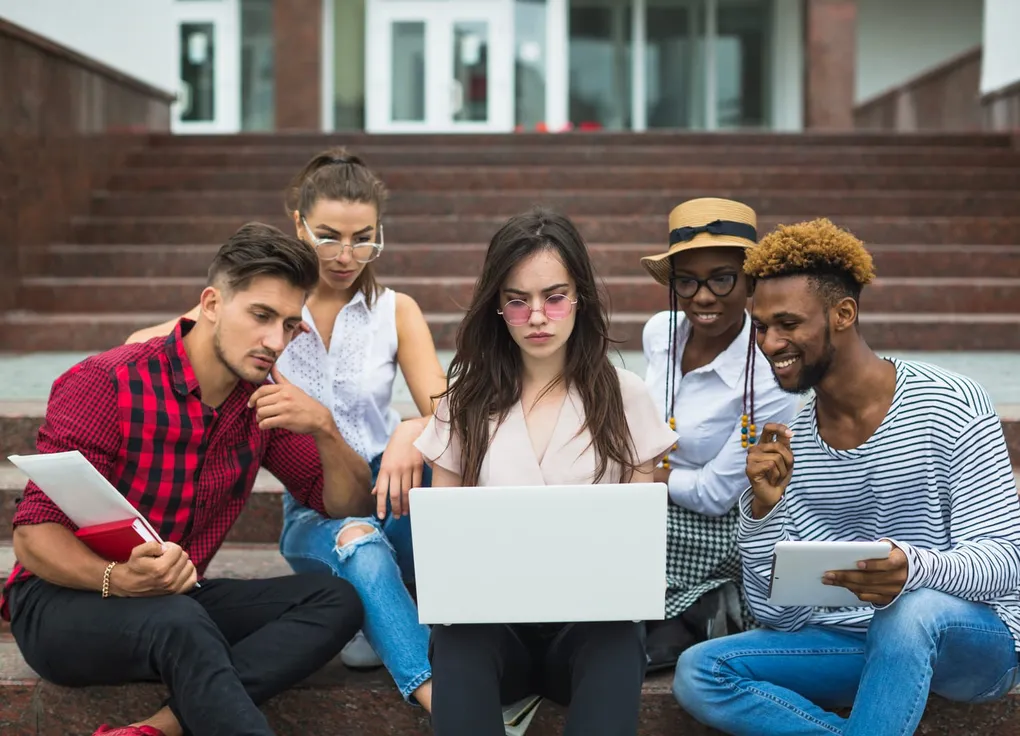 A group of students gathered around a laptop, working through a lesson together